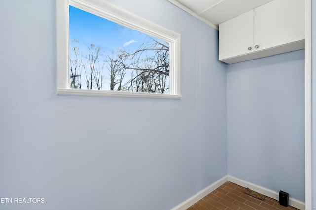 laundry area with brick floor, a wealth of natural light, cabinet space, and baseboards