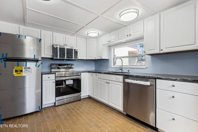 kitchen featuring appliances with stainless steel finishes, white cabinetry, a sink, and brick patterned floor