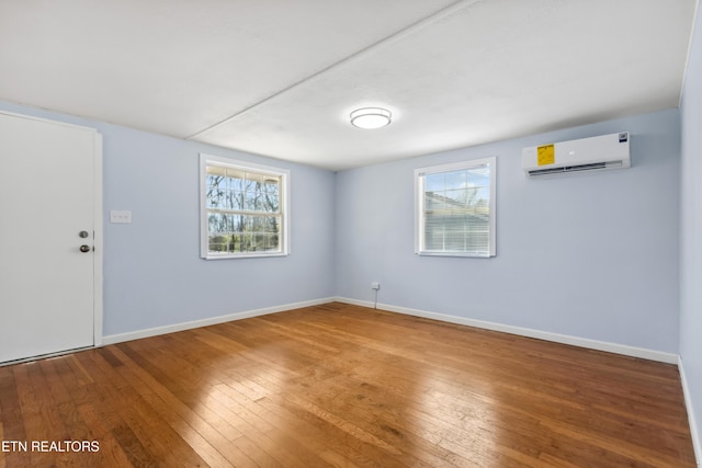 empty room featuring a healthy amount of sunlight, a wall mounted air conditioner, baseboards, and hardwood / wood-style flooring