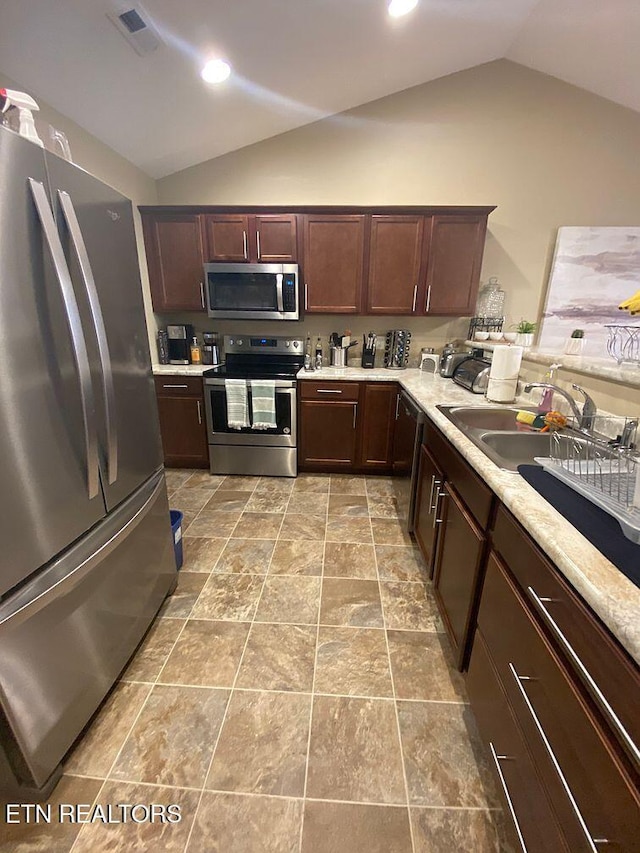 kitchen with a sink, light countertops, vaulted ceiling, and stainless steel appliances