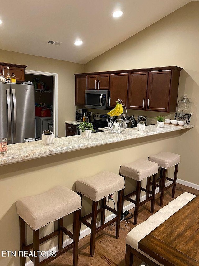 kitchen with a kitchen bar, visible vents, dark wood-type flooring, appliances with stainless steel finishes, and lofted ceiling