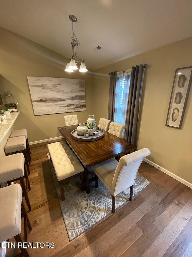 dining area with vaulted ceiling, an inviting chandelier, baseboards, and wood finished floors