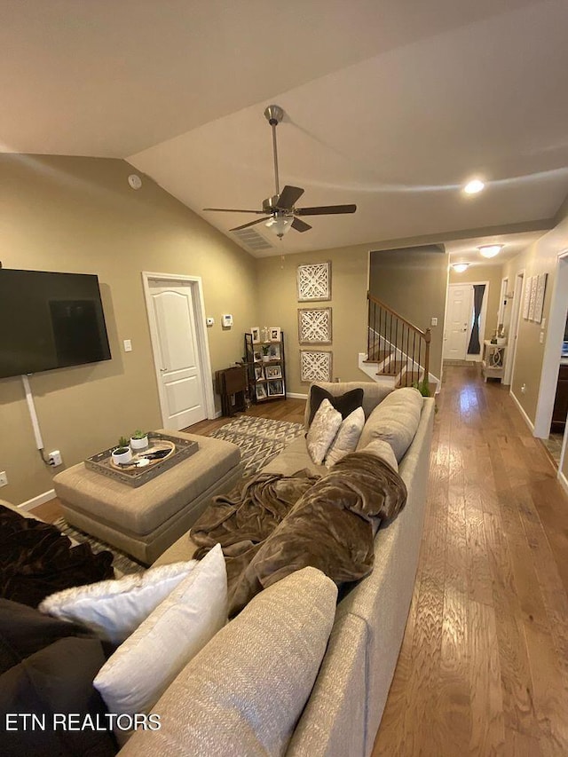 living area with baseboards, ceiling fan, stairs, vaulted ceiling, and wood-type flooring