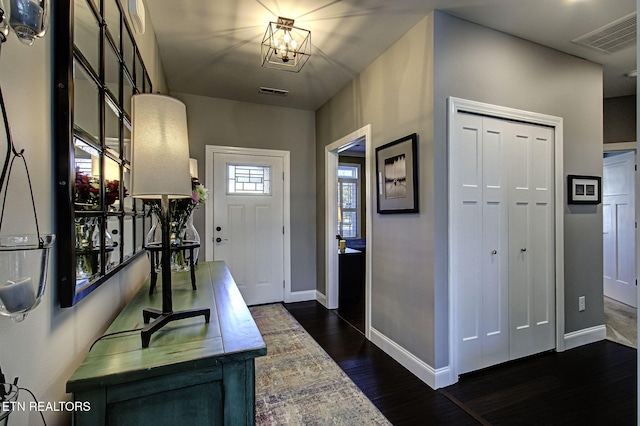 entryway with dark wood-style floors, baseboards, visible vents, and an inviting chandelier