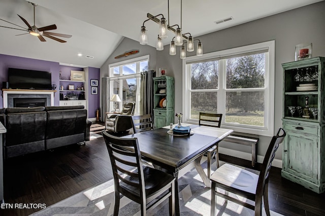 dining room with dark wood-style floors, a fireplace, visible vents, and vaulted ceiling