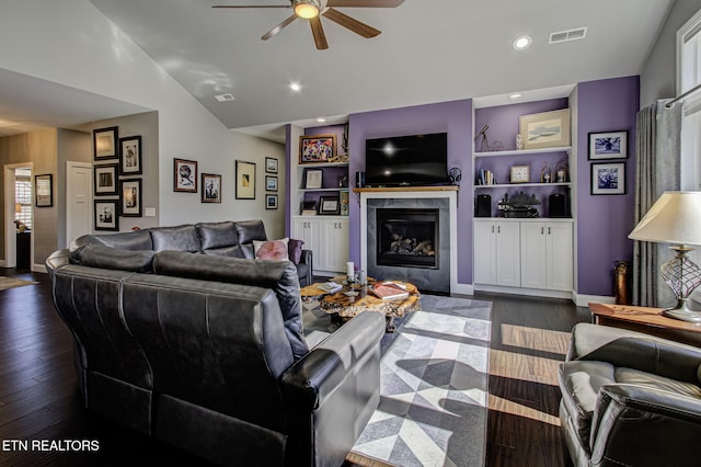 living room featuring lofted ceiling, visible vents, dark wood-type flooring, a glass covered fireplace, and a ceiling fan