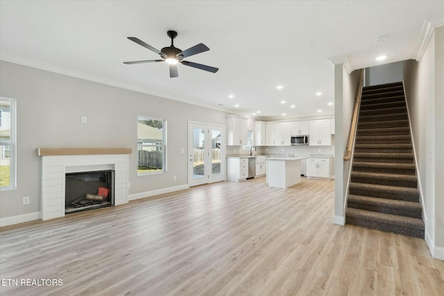 unfurnished living room featuring light wood finished floors, baseboards, stairs, and ornamental molding