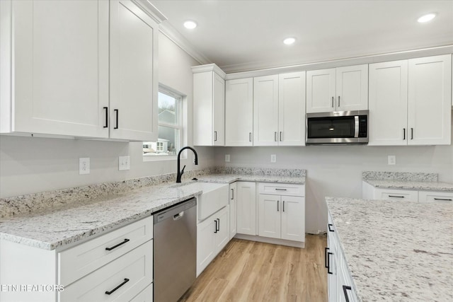 kitchen with light wood-style flooring, appliances with stainless steel finishes, light stone counters, white cabinetry, and a sink