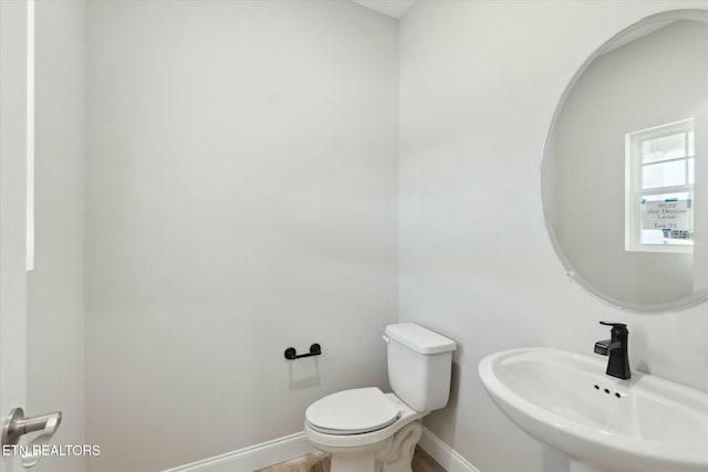 half bathroom featuring toilet, baseboards, a sink, and wood finished floors