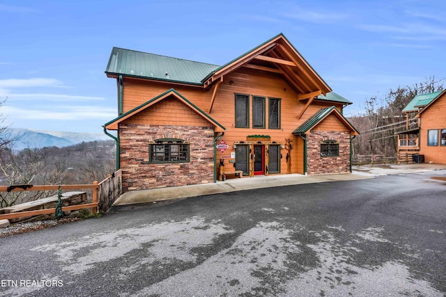 rustic home with stone siding, fence, a mountain view, and metal roof