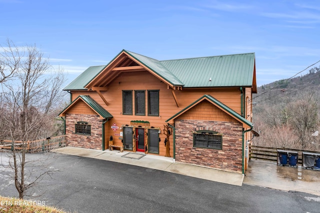 chalet / cabin with metal roof, stone siding, and fence