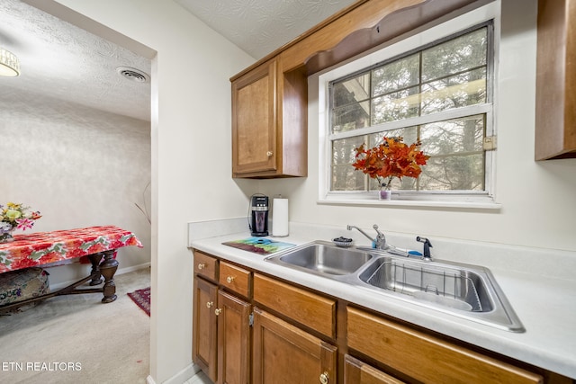 kitchen with light countertops, brown cabinetry, a sink, and visible vents