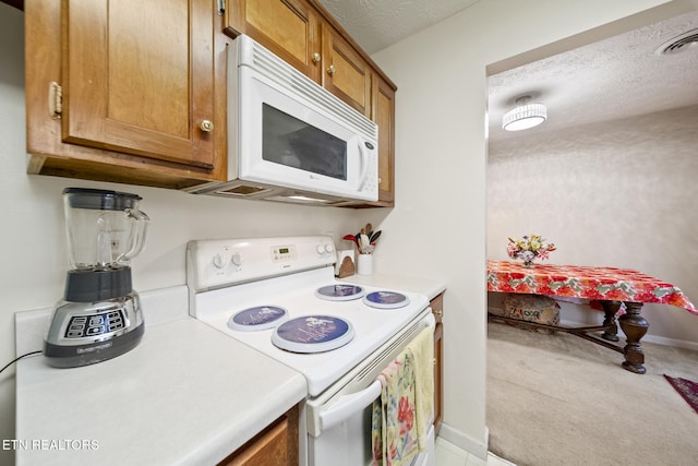 kitchen featuring brown cabinets, light countertops, visible vents, a textured ceiling, and white appliances