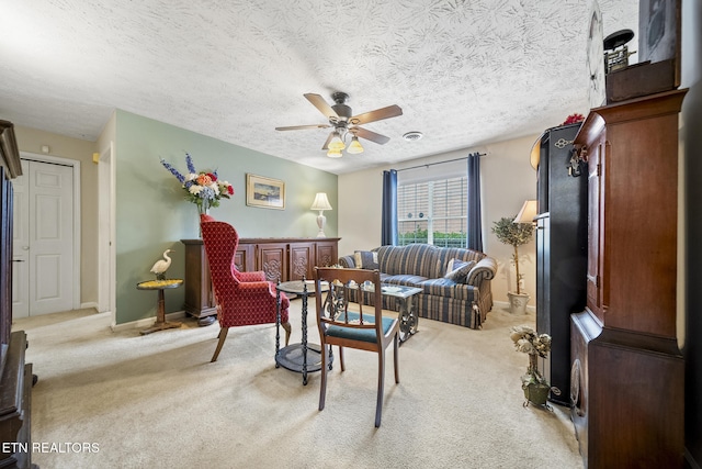 living area with a textured ceiling, baseboards, a ceiling fan, and light colored carpet