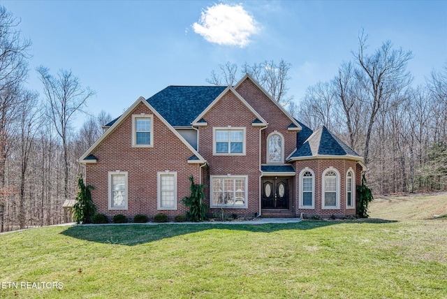 view of front of house with a front lawn, a shingled roof, and brick siding