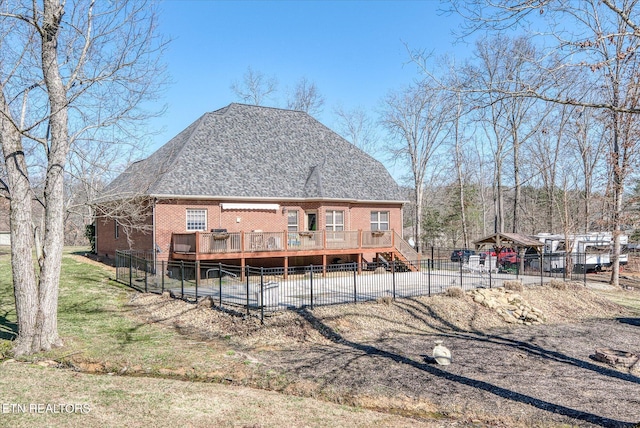 rear view of property featuring roof with shingles, fence, a deck, and brick siding