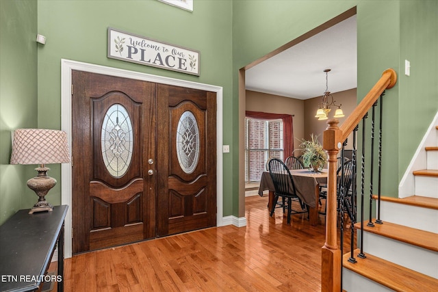 foyer entrance featuring light wood finished floors, baseboards, stairway, and a notable chandelier