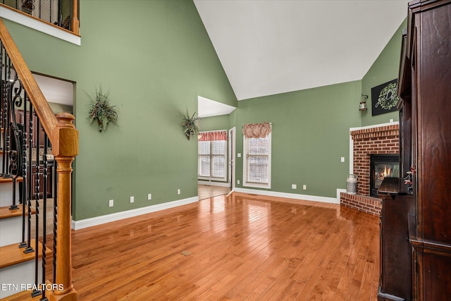 unfurnished living room with high vaulted ceiling, a fireplace, wood finished floors, baseboards, and stairway