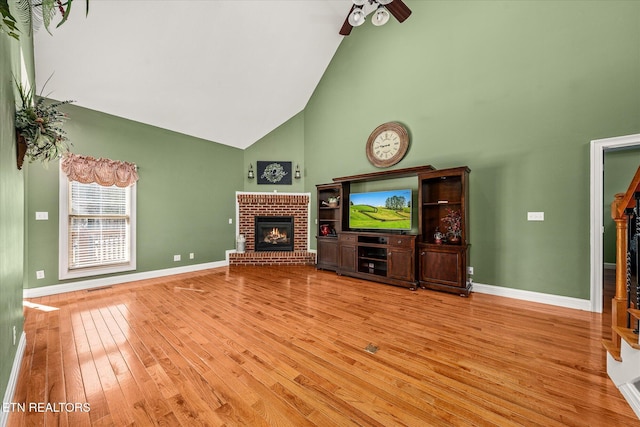 unfurnished living room with high vaulted ceiling, light wood-type flooring, a brick fireplace, and baseboards