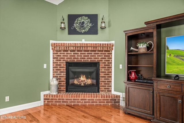 living area with a brick fireplace, baseboards, and wood finished floors