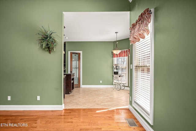 spare room with baseboards, light wood-style flooring, visible vents, and a wealth of natural light