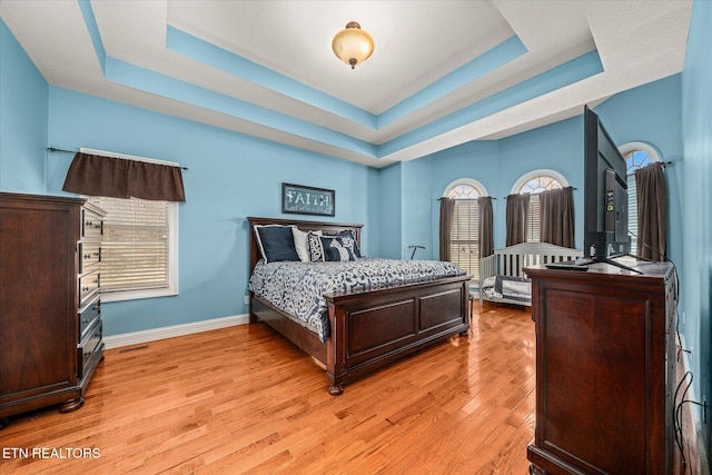 bedroom with a tray ceiling, light wood-style flooring, and baseboards