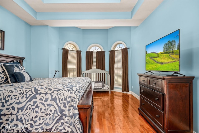 bedroom with light wood finished floors, baseboards, and a raised ceiling