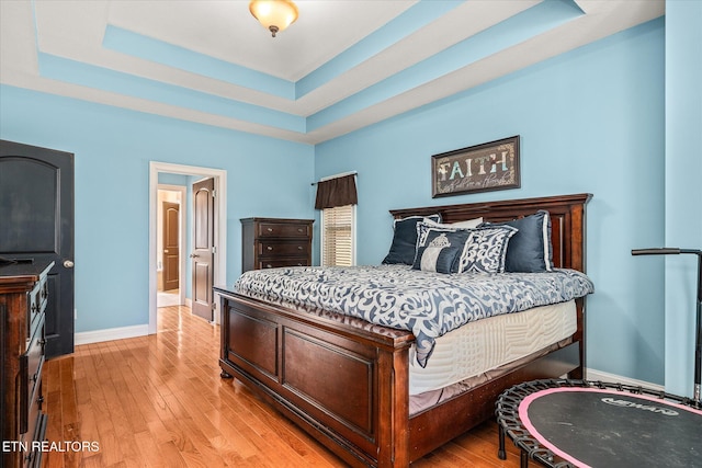 bedroom with a raised ceiling, light wood-style flooring, and baseboards