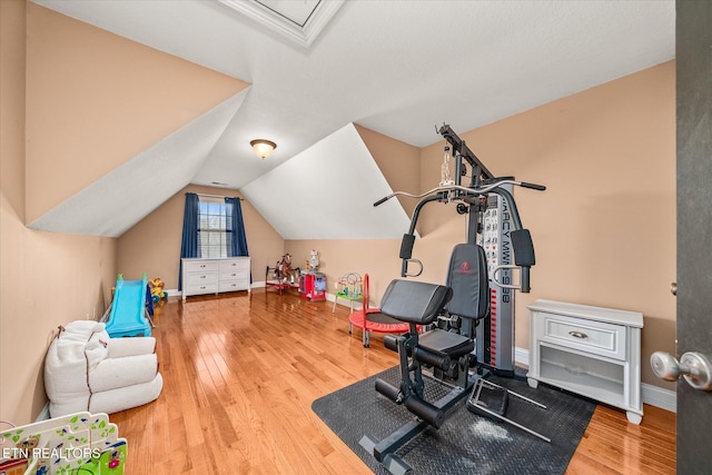 exercise room with baseboards, vaulted ceiling, and wood finished floors