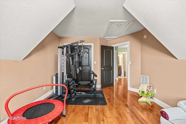 exercise area featuring attic access, baseboards, visible vents, wood finished floors, and a textured ceiling