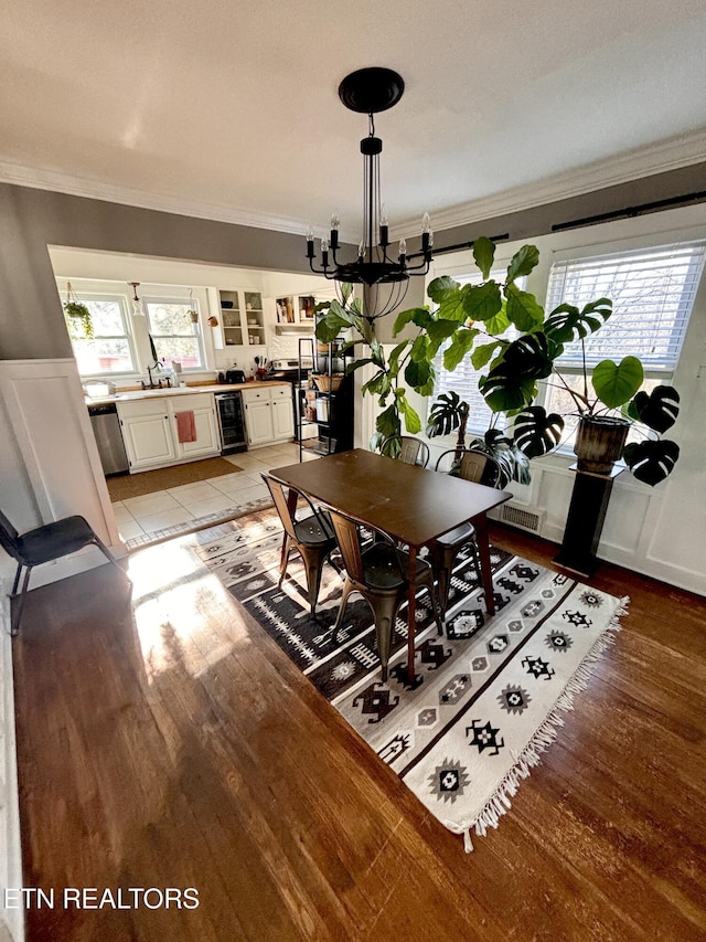 dining area featuring crown molding, wine cooler, light wood finished floors, and a chandelier