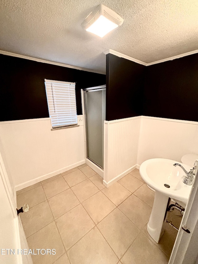 full bathroom with tile patterned floors, a textured ceiling, a stall shower, and wainscoting