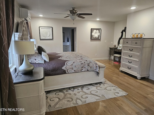 bedroom featuring ensuite bathroom, a wall unit AC, light wood-style flooring, recessed lighting, and baseboards