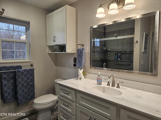 bathroom featuring toilet, a textured wall, an enclosed shower, and vanity