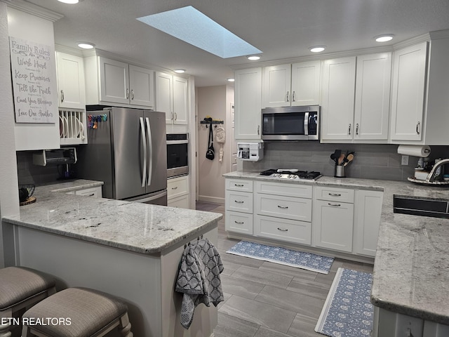 kitchen featuring a skylight, appliances with stainless steel finishes, white cabinets, a sink, and a peninsula