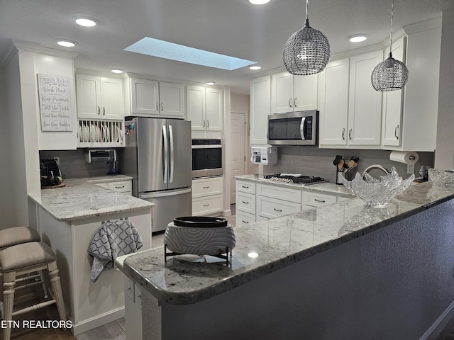 kitchen with light stone counters, a skylight, appliances with stainless steel finishes, white cabinets, and a peninsula