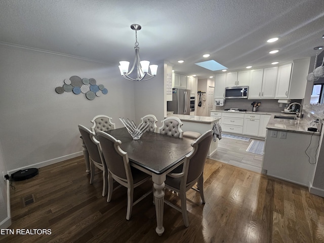 dining area featuring a skylight, visible vents, a textured ceiling, wood finished floors, and baseboards