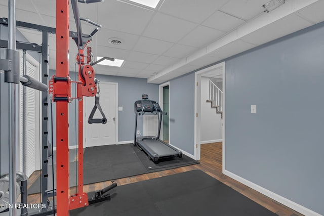 exercise room with a drop ceiling, visible vents, baseboards, and wood finished floors