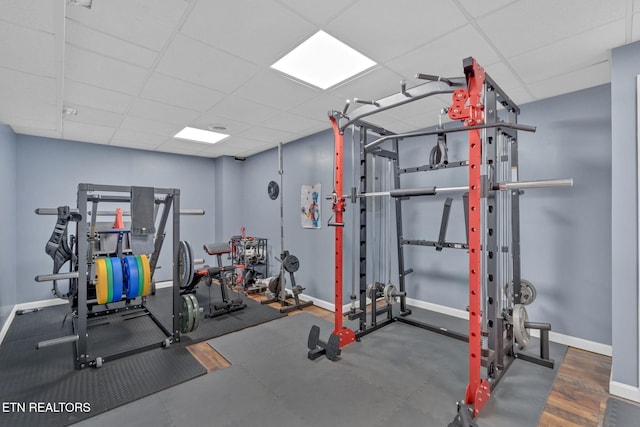 exercise room featuring a paneled ceiling and baseboards