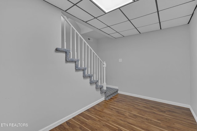 stairs with a drop ceiling, wood finished floors, visible vents, and baseboards