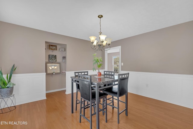 dining space featuring a wainscoted wall, light wood finished floors, and a notable chandelier