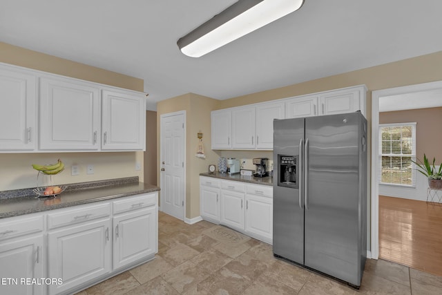 kitchen with baseboards, dark countertops, stainless steel fridge, and white cabinets