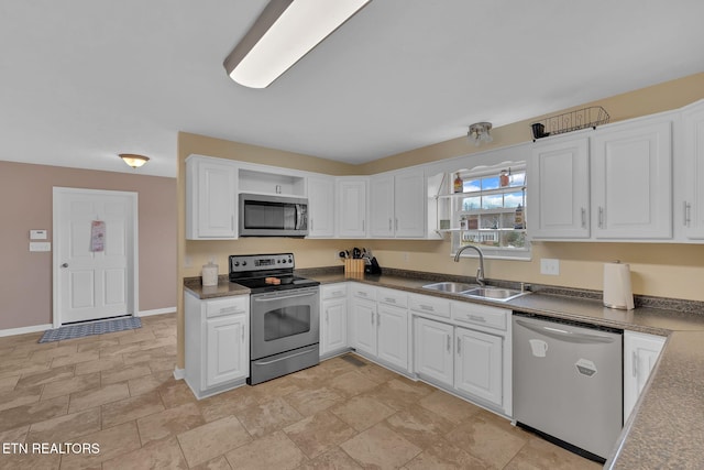 kitchen featuring baseboards, white cabinets, dark countertops, stainless steel appliances, and a sink