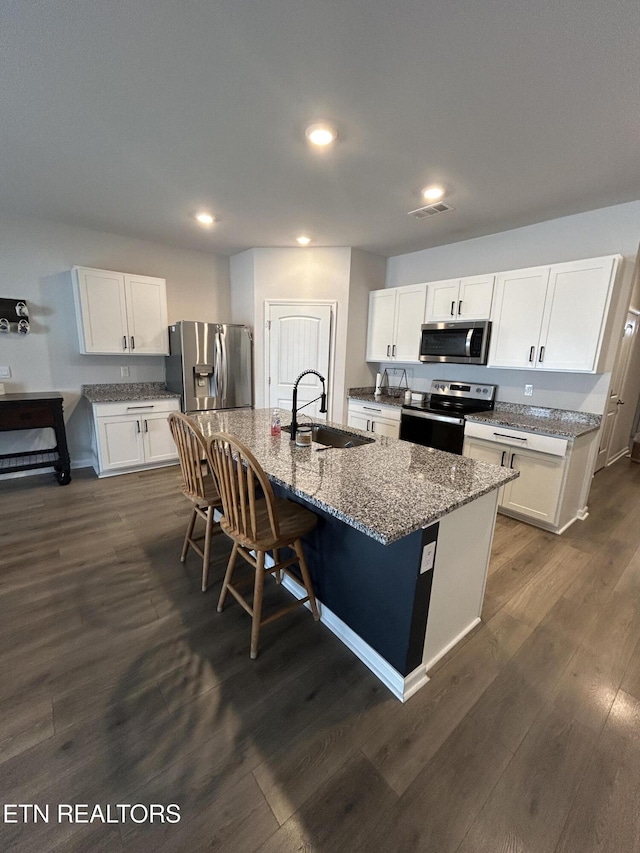 kitchen featuring visible vents, dark wood-style floors, appliances with stainless steel finishes, a kitchen island with sink, and a sink