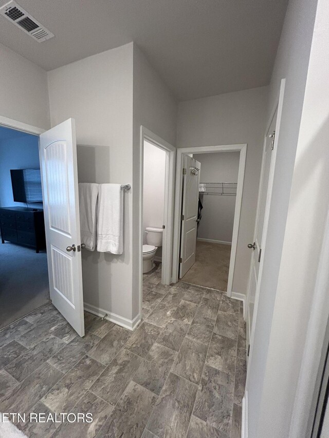 bathroom with a walk in closet, baseboards, visible vents, and toilet