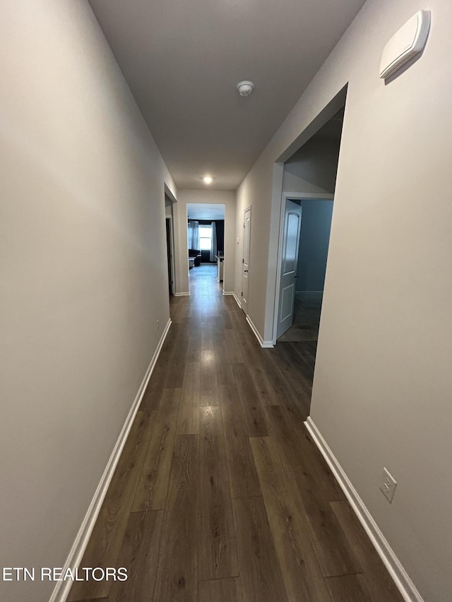 hallway featuring dark wood-style flooring and baseboards