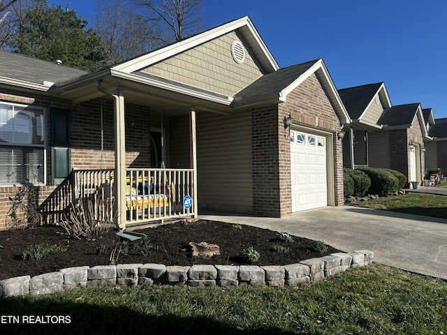 view of side of home featuring brick siding, a porch, driveway, and a garage