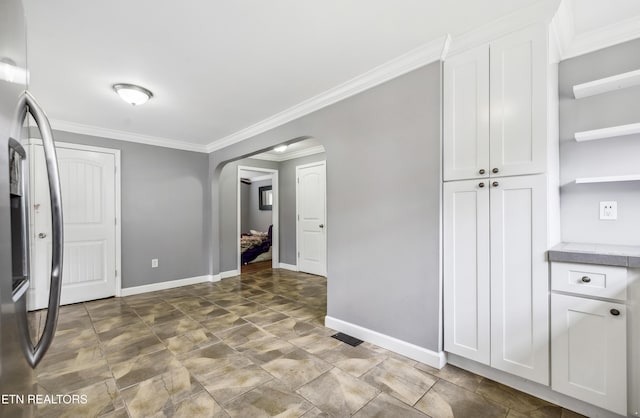 kitchen with stainless steel fridge, arched walkways, white cabinets, and ornamental molding