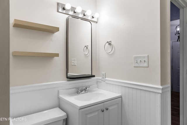 half bathroom featuring vanity, toilet, and wainscoting