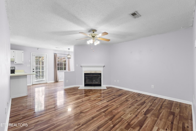 unfurnished living room with visible vents, a fireplace with flush hearth, a ceiling fan, wood finished floors, and baseboards